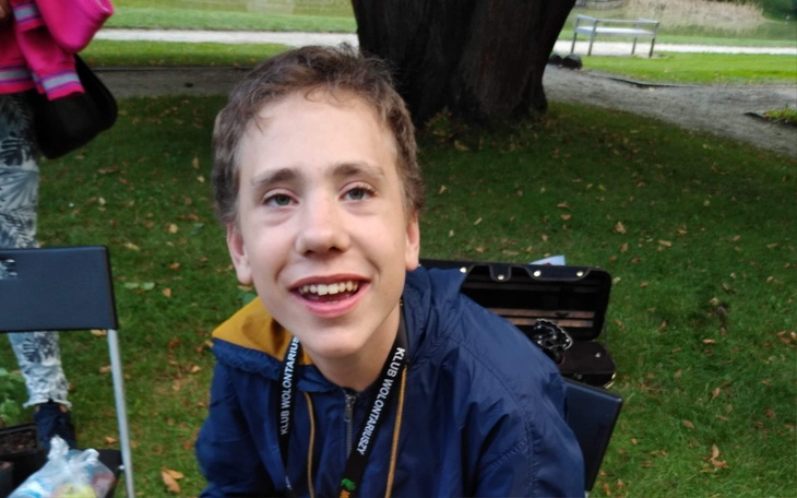 Chłopiec z uśmiechem, siedzący na trawie w parku.