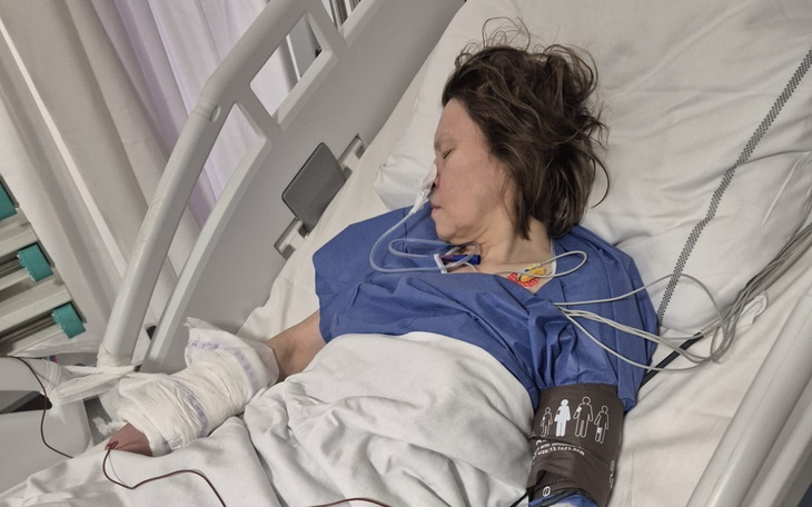 Kobieta leżąca w szpitalnym łóżku, w niebieskim fartuchu.