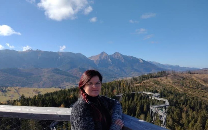 Kobieta na tle górskiego krajobrazu, w słoneczny dzień.