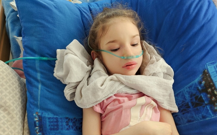 Chora dziewczynka leży w szpitalnym łóżku, podłączona do tlenu.
