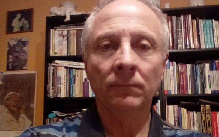 Mężczyzna w koszulce, stojący przed regałem z książkami.