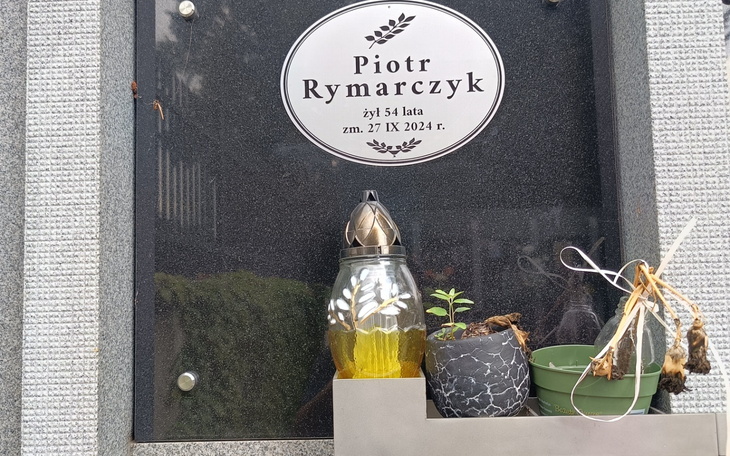 Nagrobek z imieniem Piotr Rymarczyk, z lampką i roślinami.