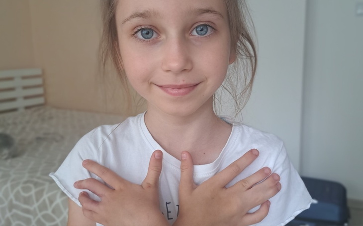 Dziewczynka z uśmiechem, trzymająca ręce na klatce piersiowej.