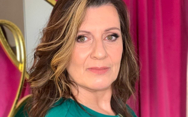 Kobieta w zielonej bluzce, pozująca na tle różowych zasłon.