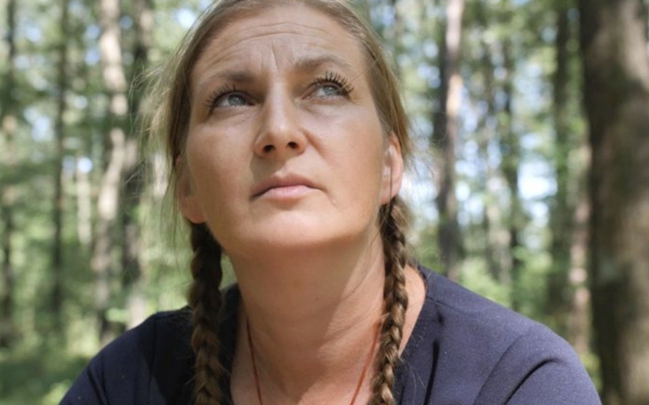 Kobieta w lesie, patrząca w górę, z warkoczami.