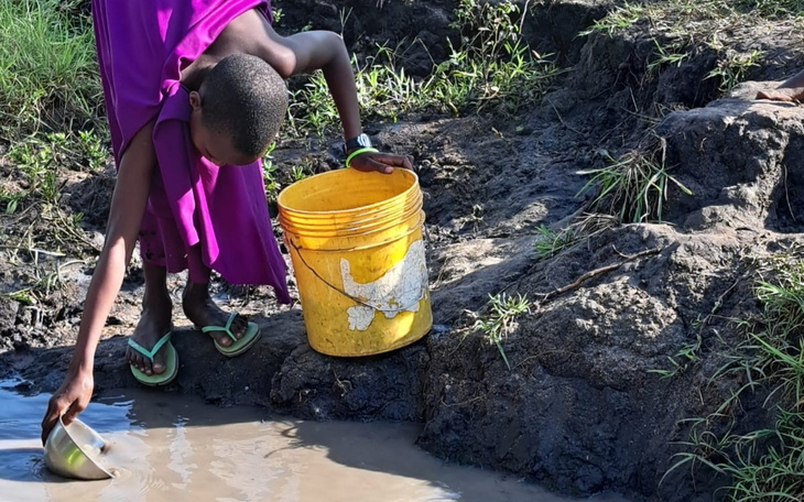 Dziecko w fioletowej sukience zbierające wodę z błotnistego miejsca.