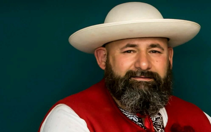 Mężczyzna w kapeluszu, uśmiechający się na tle zielonej ściany.