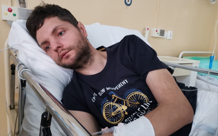 Mężczyzna leżący w szpitalnym łóżku, z opatrunkiem na ręce.