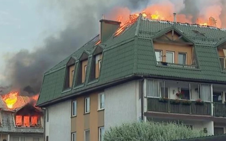 Dach budynku w płomieniach, dym unoszący się w powietrzu.