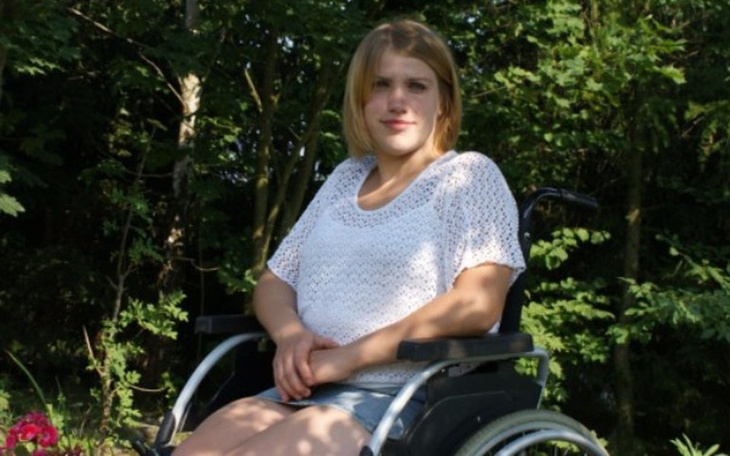 Młoda dziewczyna w wózku inwalidzkim w otoczeniu natury.