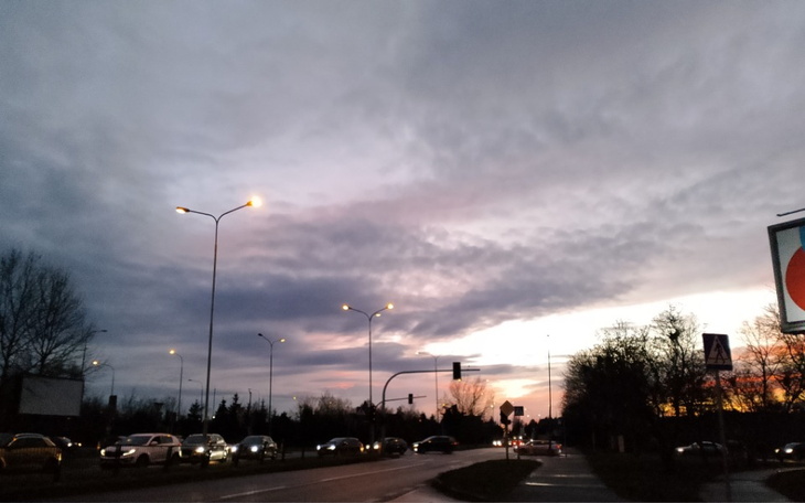 Zachód słońca nad miastem, widok na ulicę z latarniami.