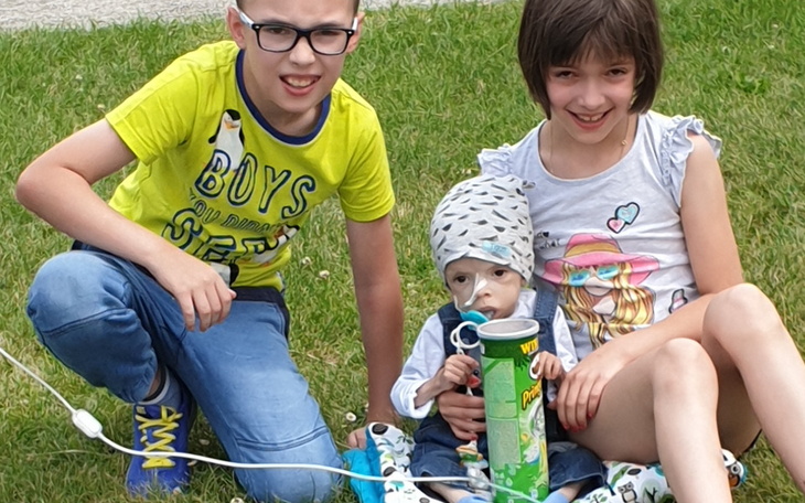 Dzieci bawiące się na trawie, jedno z nich trzyma napój.