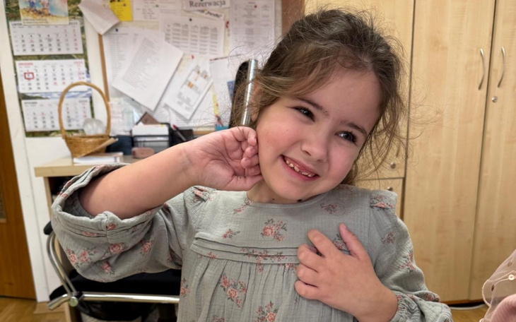 Mała dziewczynka w szarej bluzce, uśmiechająca się i pozująca do zdjęcia.