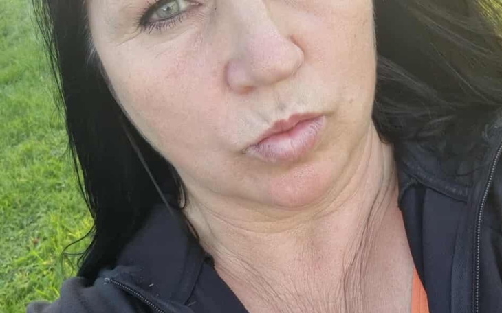 Kobieta z długimi włosami, robiąca selfie na tle zieleni.