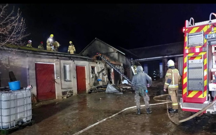 Strażacy gaszący pożar w nocy przy budynku.
