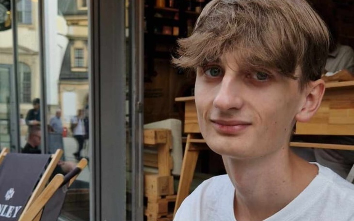 Młody mężczyzna siedzący w kawiarni, uśmiechający się do kamery.