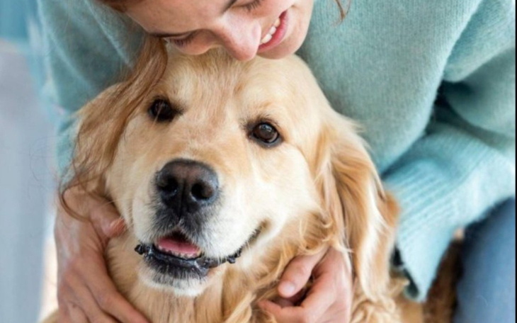 Kobieta przytula złotego retrievera, oboje uśmiechnięci.