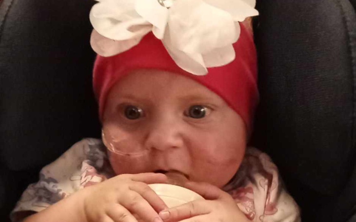 Mała dziewczynka w czerwonej czapce z białą kokardą trzyma kubek.