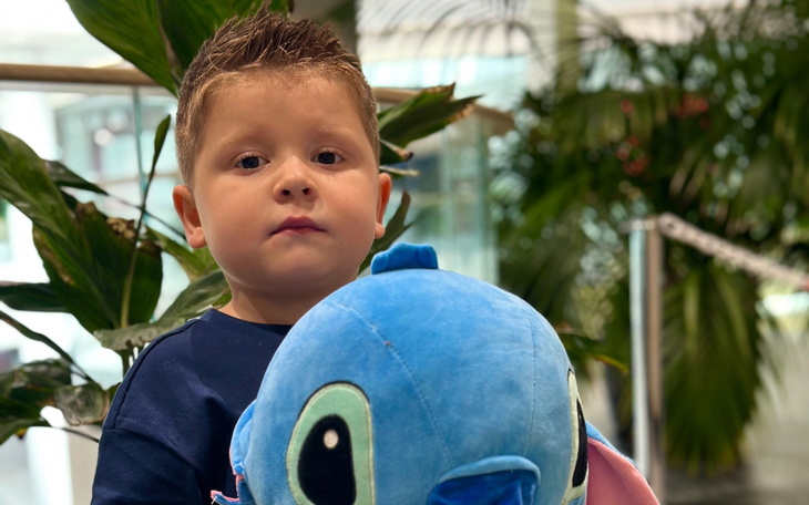 Chłopiec trzymający pluszowego Stitcza, w tle rośliny.