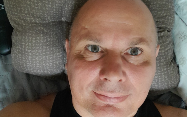 Mężczyzna leży na poduszce, patrząc w kamerę.