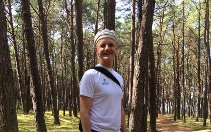 Mężczyzna w lesie, uśmiechający się do kamery.