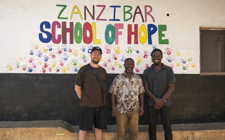 Trzech mężczyzn przed muralem 'Szkoła Nadziei' na Zanzibarze.