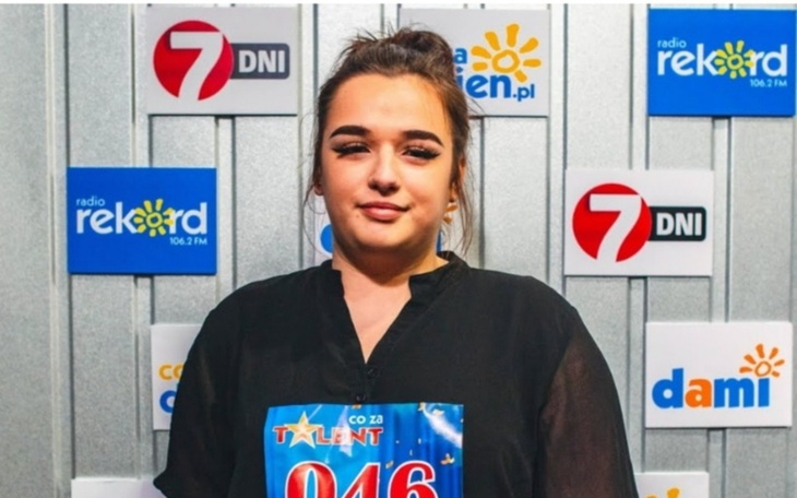Młoda kobieta na scenie, trzymająca numer w konkursie talentów.