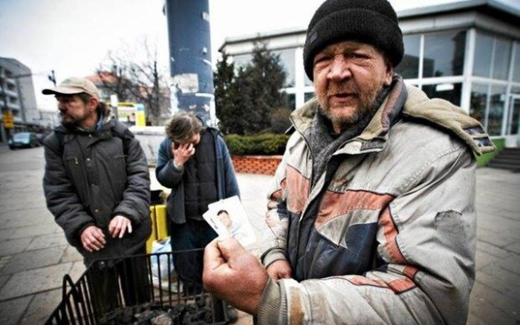 Bezdomny mężczyzna trzymający zdjęcie, w tle inni ludzie.