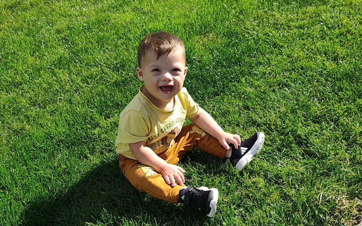 Mały chłopiec siedzi na trawie, uśmiechając się radośnie.