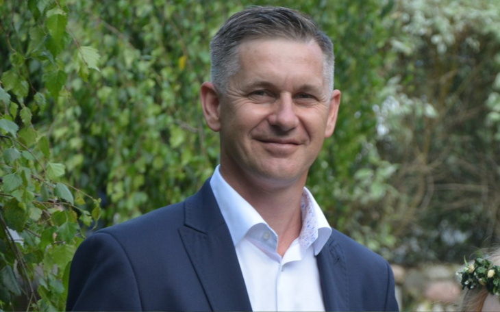 Mężczyzna w garniturze uśmiechający się w plenerze.