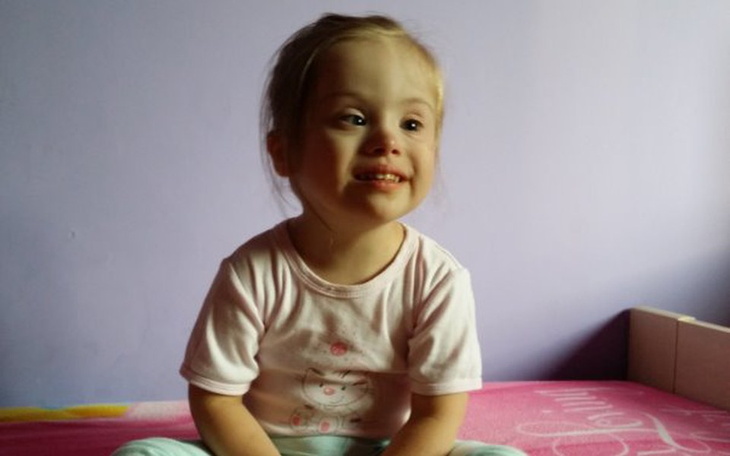 Uśmiechnięta dziewczynka siedząca na łóżku w różowej koszulce.