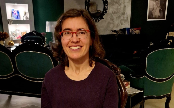 Uśmiechnięta kobieta w okularach, siedząca w eleganckim wnętrzu.