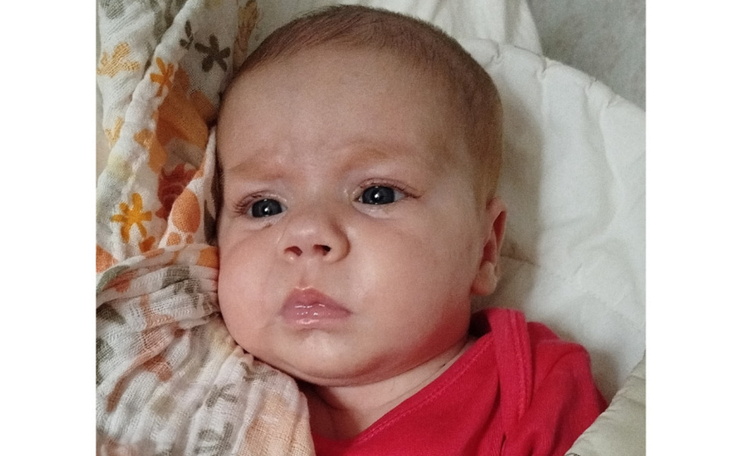 Noworodek leżący na poduszce, z wyrazem twarzy.