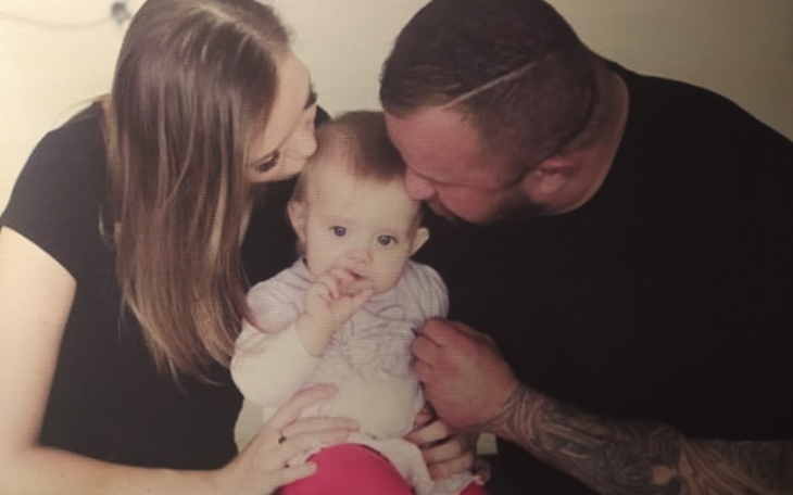 Rodzina z małym dzieckiem, wszyscy uśmiechnięci i blisko siebie.