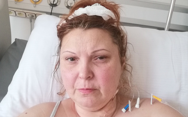 Kobieta leżąca w szpitalnym łóżku, z widocznymi rurkami i smutnym wyrazem twarzy.