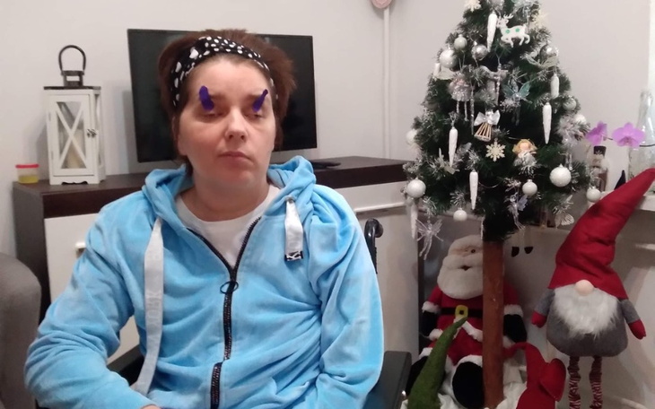 Kobieta w niebieskiej bluzie siedzi obok choinki i dekoracji świątecznych.