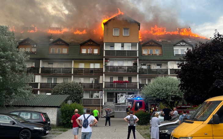 Pożar na dachu budynku, ludzie obserwują akcję ratunkową.