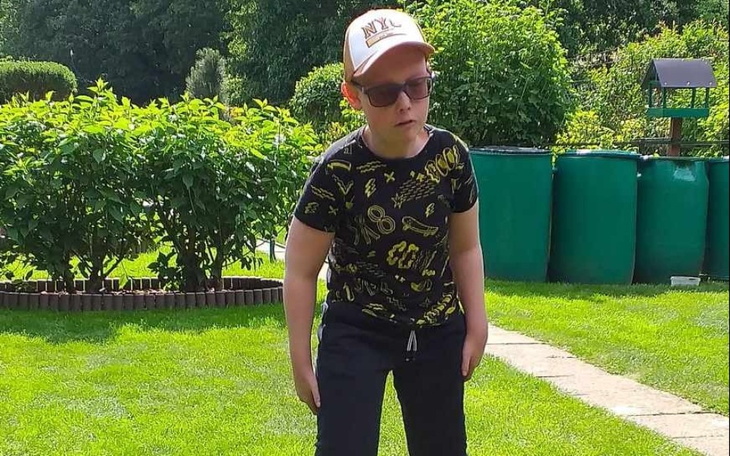 Chłopiec w okularach przeciwsłonecznych na trawie, w letnim stylu.