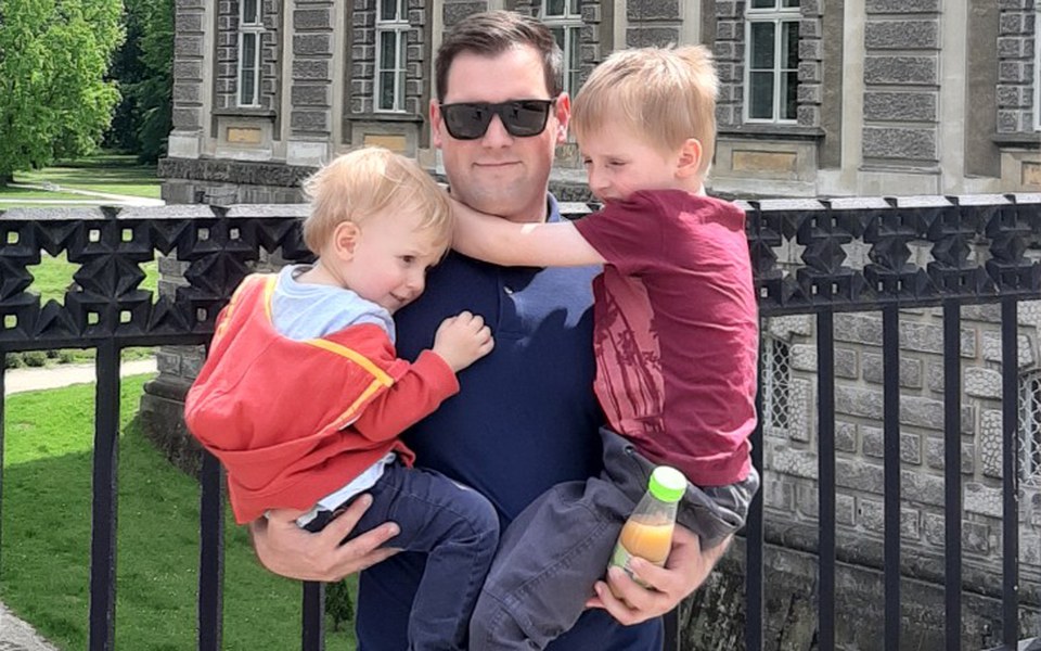 
        Tata trzymający dwoje dzieci, spędzający czas na świeżym powietrzu.
    