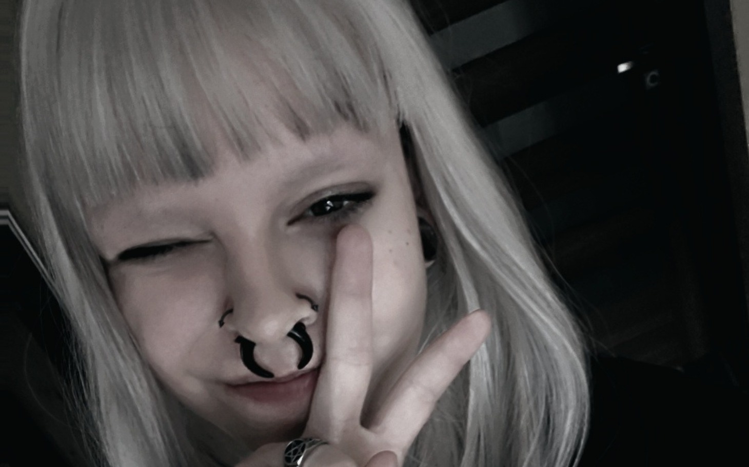 
        Młoda kobieta z białymi włosami robi znak pokoju w ciemnym otoczeniu.
    