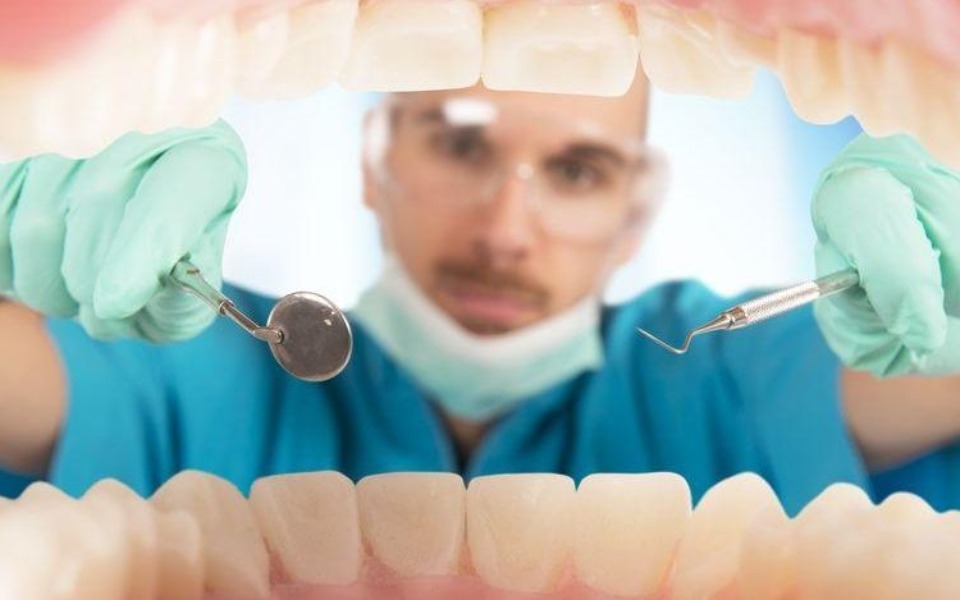 
        Dentysta trzymający narzędzia w otwartej jamie ustnej.
    