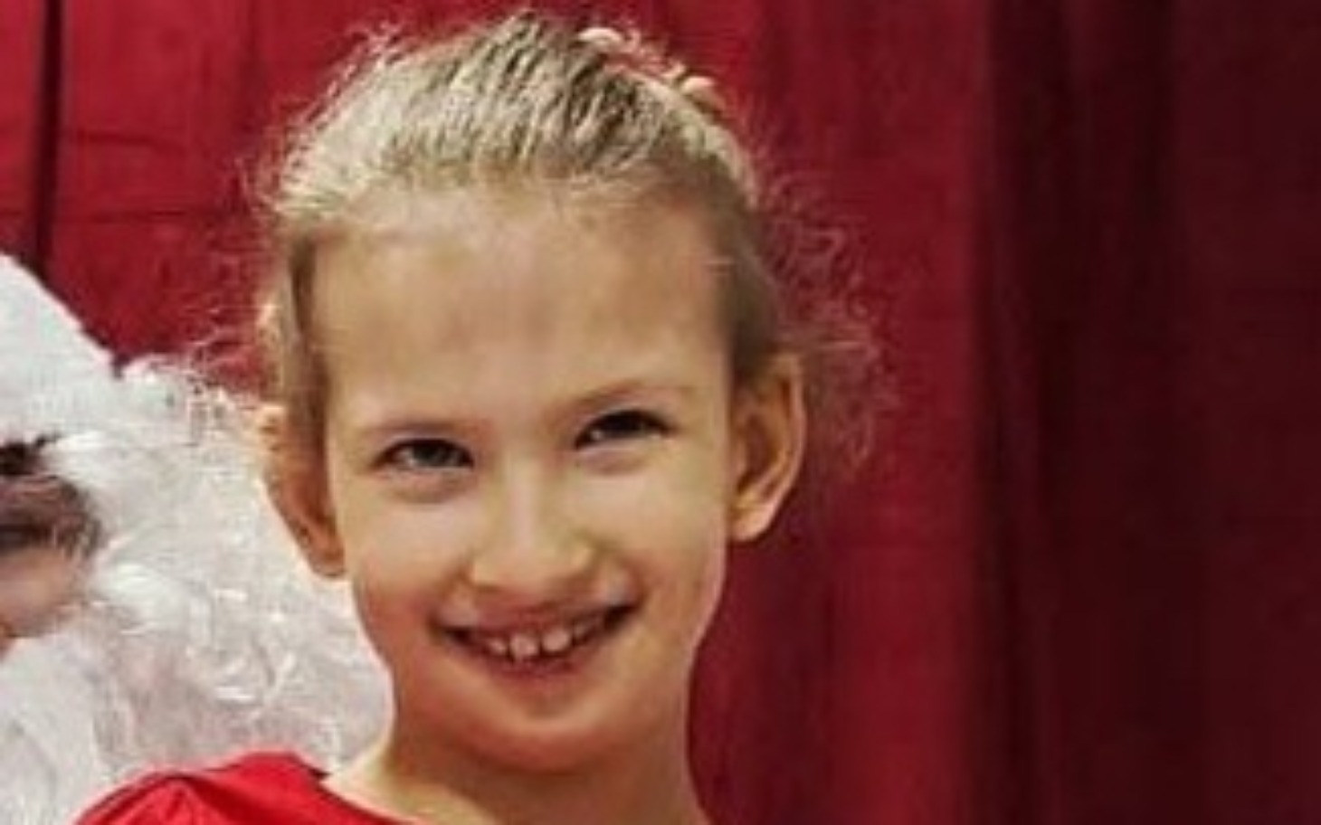 
        Uśmiechnięta dziewczynka w czerwonej sukience, pozująca na tle.
    