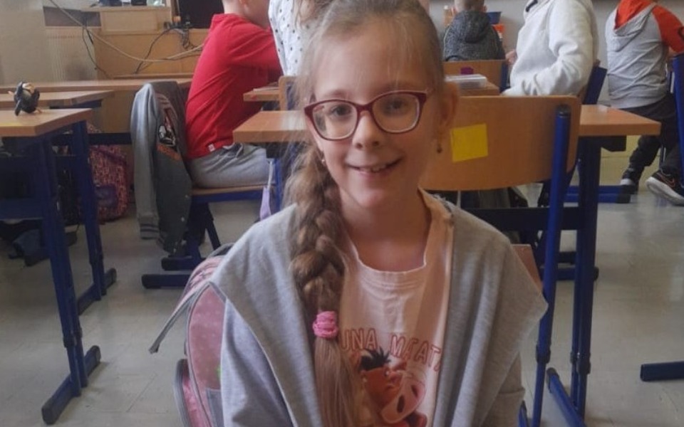 
        Uśmiechnięta dziewczynka w klasie, z okularami i warkoczem.
    
