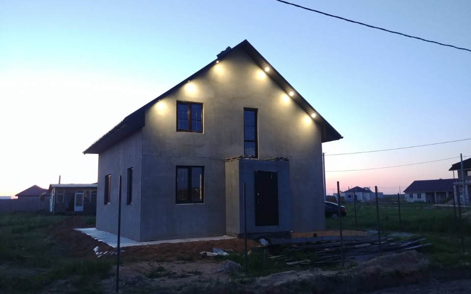 
        Nowoczesny dom w trakcie budowy, oświetlony wieczorem.
    