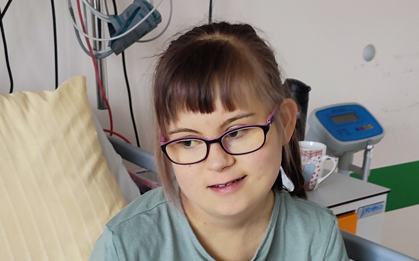 
        Młoda dziewczyna w szpitalu, nosząca okulary i uśmiechająca się.
    