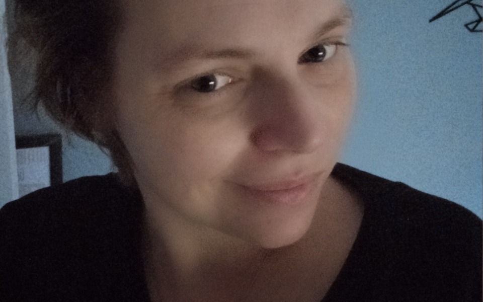 
        Kobieta z uśmiechem, w ciemnym ubraniu, na tle niebieskiej ściany.
    