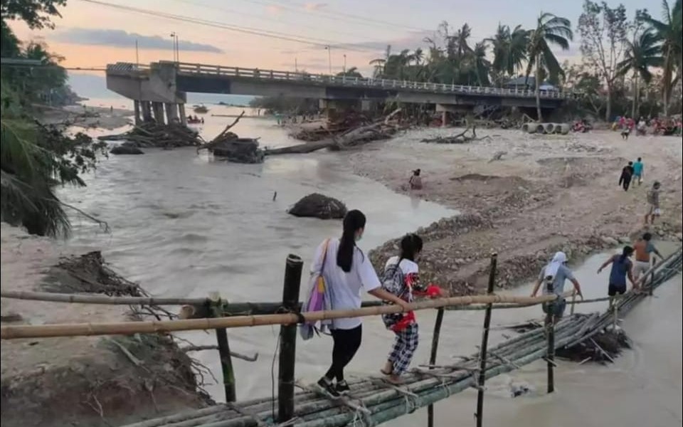 
        Zniszczony most po powodzi, ludzie przechodzą przez prowizoryczny most.
    