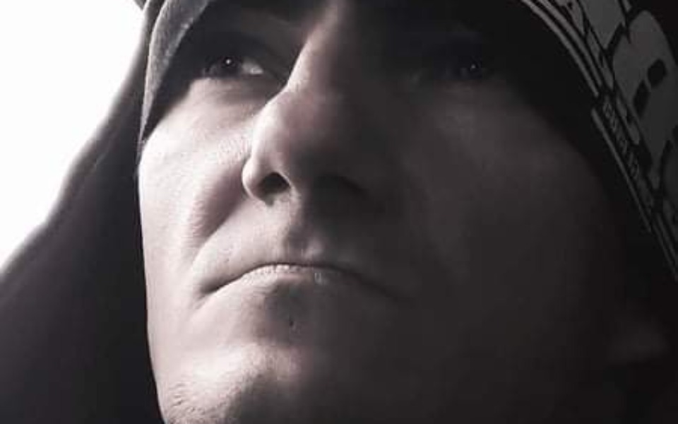 
        Mężczyzna w kapturze, z poważnym wyrazem twarzy.
    