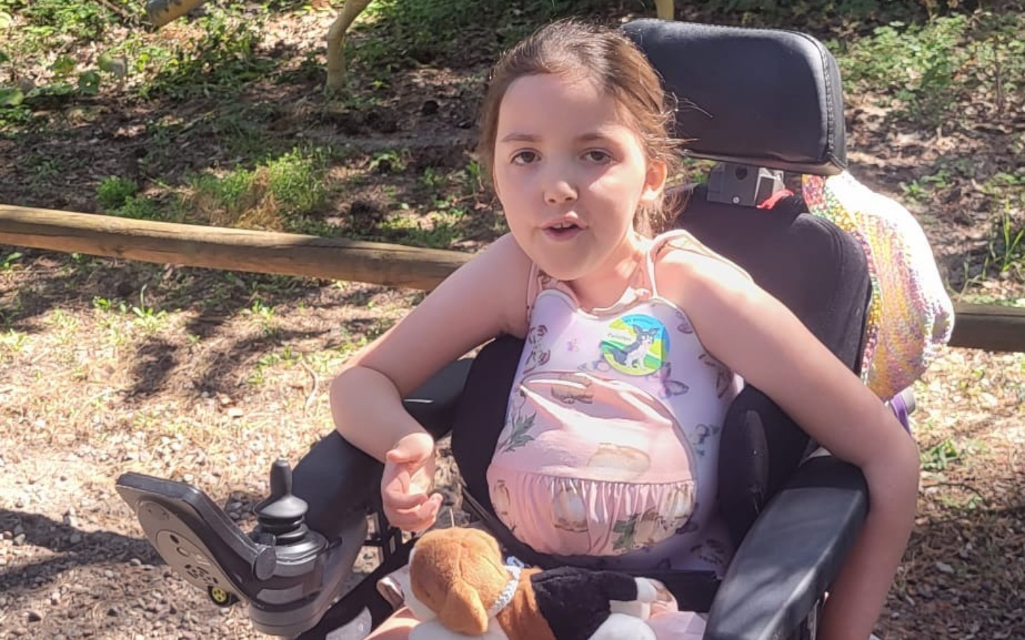 
        Dziewczynka w wózku inwalidzkim, uśmiechająca się z pluszowym zwierzątkiem.
    