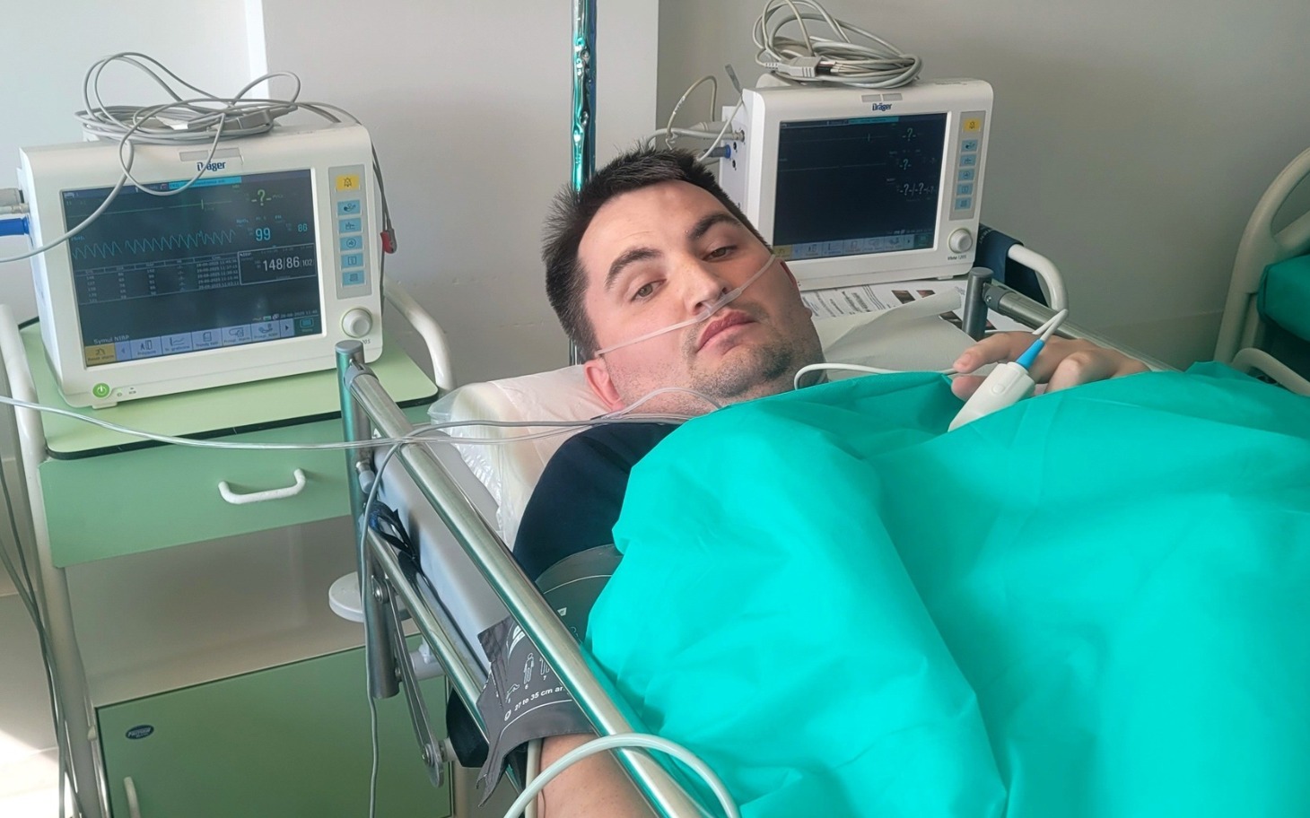 
        Mężczyzna leżący w szpitalu, podłączony do monitorów medycznych.
    